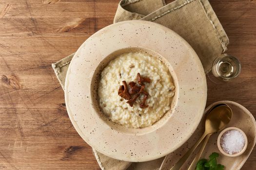 Risoto with chanterelle mushrooms in large plate. Traditional italian dish. Wooden old table, spoons, napkin. Classic hot dish of rice, cheese and wine. Top view, copy space