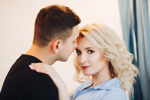 Close up of happy couple embracing each other. Beautiful blonde girlfriend in blue looking at camera, handsome boyfriend in black touching face to face. Romantic moment.