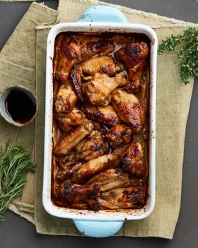 Barbecue chicken wings. Slow cooker sweet and spicy. Oven baked marinated chiken in blue ceramic tray with brush in bbq red sauce. Dark rustic table. Top view, vertical