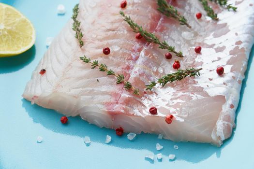 Fillet of raw white walleye fish on a blue plate on a white background. Whole piece of fresh fish with herbs and lemon, side view