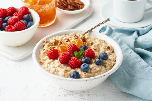 Oatmeal porridge with blueberry, raspberries, jam and nuts in white bowl, dash diet with berries, white background, side view. Healthy diet breakfast