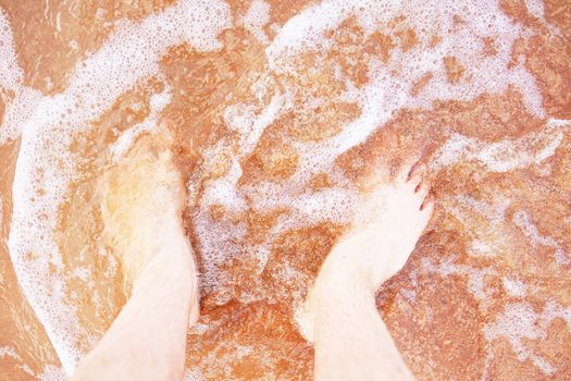 Bare men's feet are washed by sea wave. Walk along ocean. Summer vacation.