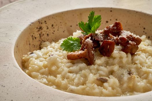 Risoto with chanterelle mushrooms in large plate. Traditional italian dish. Wooden old table, spoons, napkin. Classic hot dish of rice, cheese and wine. Side view, close up