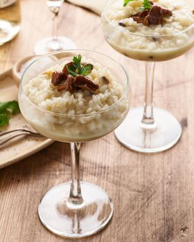 Risotto with mushrooms in wine glass. Unconventional unusual serving. Rice porridge with mushrooms. Wooden old table. Hot dish in glass bowl. Side view, vertical