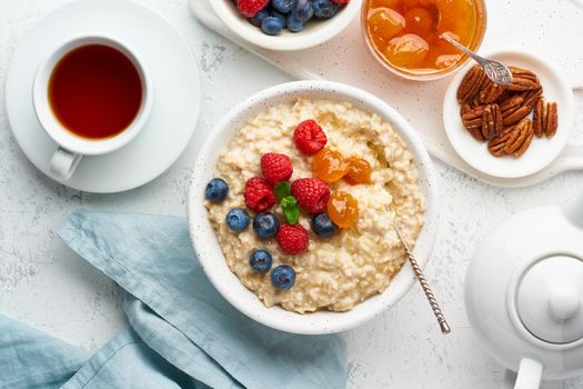 Oatmeal porridge with blueberry, raspberries, jam and nuts in white bowl, dash diet with berries, white background, top view. Healthy diet breakfast