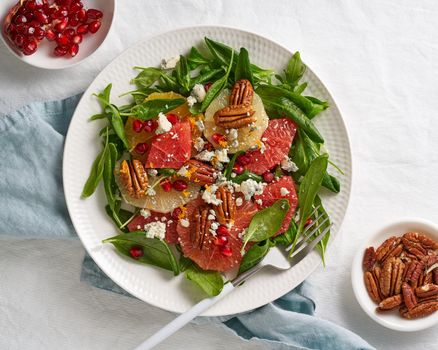 Fruits citrus salad with nuts, green lettuce leaves. Balanced food. Spinach with orange, grapefruit, pecans and gorgonzola, garnished with pomegranate seeds, top view