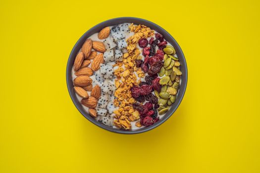 Mango smoothies bowl with almond, dragon fruit, dried cherries, pumpkin seeds and granola on yellow background.