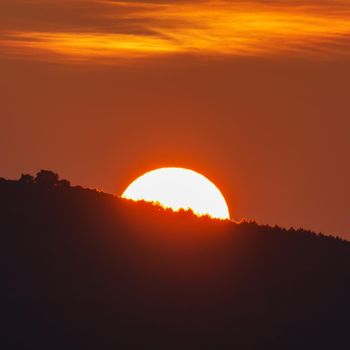 Long shot of sun behind mountain at sunrise