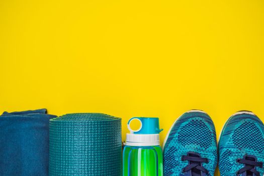 Everything for sports turquoise, blue shades on a yellow background. Yoga mat, sport shoes sportswear and bottle of water. Concept healthy lifestyle, sport and diet. Sport equipment. Copy space.