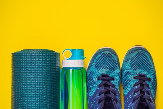 Everything for sports turquoise, blue shades on a yellow background. Yoga mat, sport shoes sportswear and bottle of water. Concept healthy lifestyle, sport and diet. Sport equipment. Copy space.