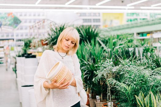 Gardening, planting and shopping concept. Beautiful mature adult woman choosing houseplants and pots in greenhouse or garden centre. Senior buying flowers plants at market store in mall.