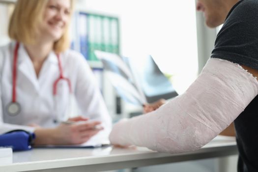 Male patient with bandage on his arm sitting at traumatologist appointment closeup. First aid for fractures and injuries of limbs concept