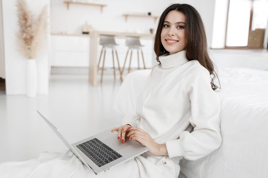 young woman working in laptop at home indoor in white colours. High quality photo