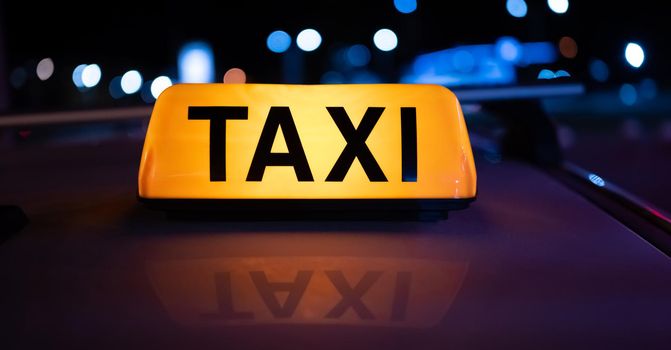 Taxi car light on dark street at night with illumination. Cab sign on the vehicle roof closeup glowing in the dusk
