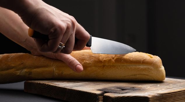 French baguette for bruschettas cut with knife on wooden board by woman hands. Rustic crusty bread loaf for teraditional snacks