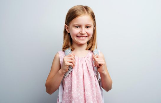 Portrait of primary school girl with backpack on gray background