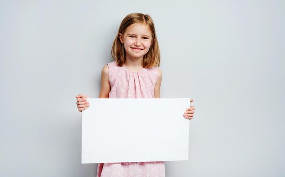 School girl holding horizontal blank white poster on a grey wall background