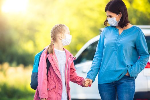 Little girl going back to school with mother through car parking during coronavirus pandemic