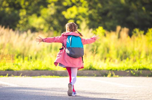 Rear view of little girl wearing backpack running with open arms after school on sunny parking