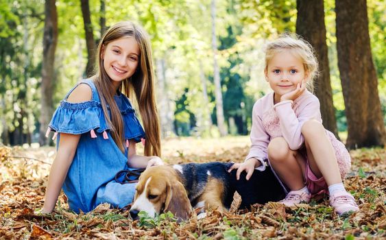 Young sisters playing with beagle dog in leaves