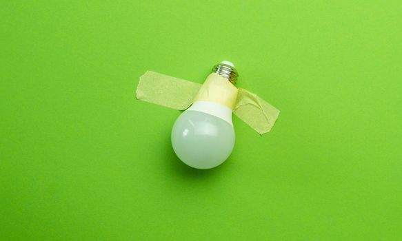 Lamp lightbulb attached with tape on green background. Concept of creativity and invention