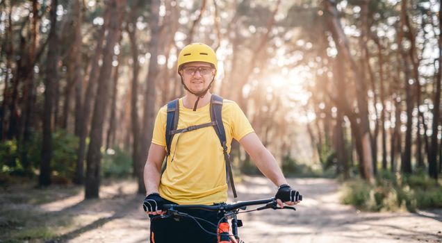 Happy cyclist standing with bike in pine forest
