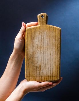 Hand holding toy wooden board desk for cooking. Craft kitchenware for meal preparing on blue background