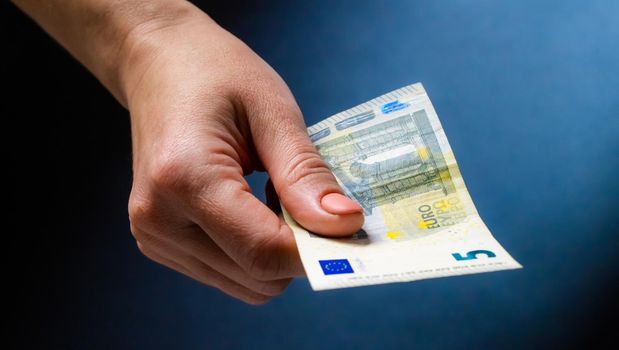Hand holding five euro banknote. European currency in cash and person with money