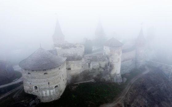 Ancient fortress towers in Kamenets-Podolsky, Ukraine in foggy weather from aerial view with landscape. Medieval old castle bastion with scenic towers in clouds from drone