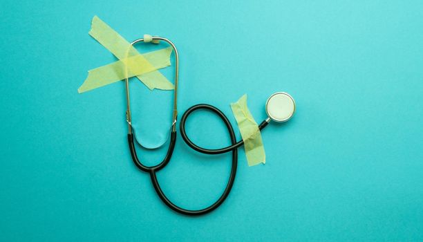 Medical stethoscope for examing heart deseases attached with tape on light blue background. Concept of cardiology help, healthcare system and wellness