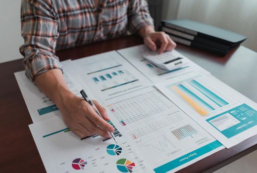 Businessman calculates and analysis chart statistics about tax, accounting, math finance, on wooden desk in the office.