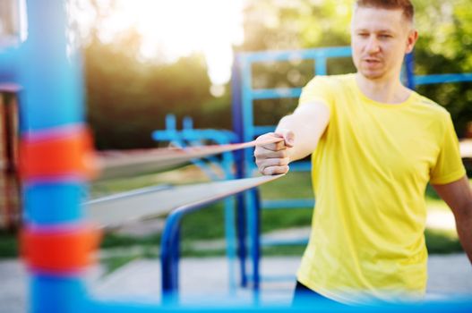 Sportive man training with resistance band outdoors in park