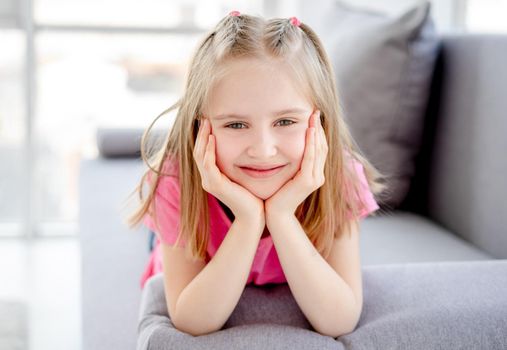 Happy little girl resting on sofa with head on hands indoors