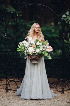 Adorable elegant, sensual young woman looking down and holding wedding flowers boquet. Front view horizontal picture of beautiful blond makeup bride in wedding dress full of love posing on camera.