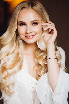 Portrait of beautiful and charming blondie bride, looking and smiling at camera. Beautiful sexy lady with pure skin, long hair posing in morning at bedroom. Wedding concept and preparing.