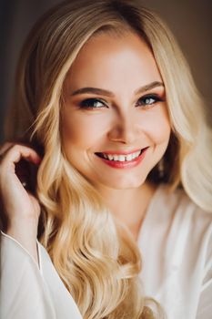 Beautiful and sensuality blondie bride sitting in bedroom, dreaming with closed eyes. Young and sexy woman with long curly hair and perfect make up, wearing in lace lingerie. Morning before wedding.