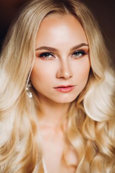 Portrait of confident and seductive blondie bride seriously looking at camera. Beautiful sexy lady with wavy long hair and perfect make up and long earrings. Morning of beautiful bride.