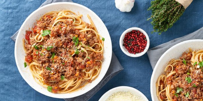 Pasta Bolognese spaghetti. Long banner with Fettuccine, mincemeat and tomatoes, parmesan cheese in plate. Italian dinner for two, dark blue tablecloth. Top view