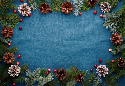 Christmas and Happy New Year dark blue background. Frame with fir branches, cones, cranberry berries. Textile backdrop with copy space.