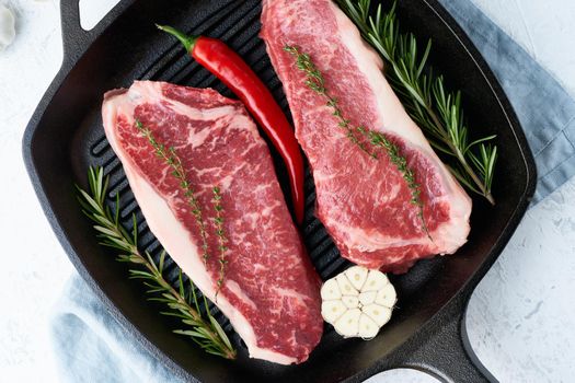 Two fresh raw big whole pieces of meat, beef fillet, marble striploin in cast-iron large pan. Top view, close up. Seasoning steak with salt.