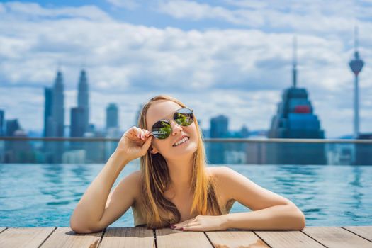 Young woman in outdoor swimming pool with city view in blue sky.