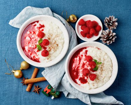 Rice pudding. Christmas food. French milk rice dessert with raspberries, blueberries, berries, jam. Healthy Vegan diet breakfast with coconut milk, cinnamon. Blue linen textile. Dark background.