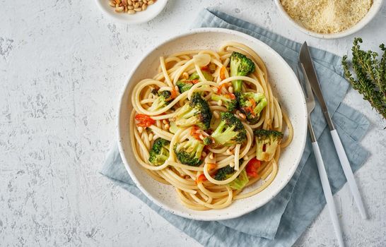 Spaghetti pasta with broccoli, bucatini with peppers, garlic, pine nuts. Food for vegans, vegetarians. Healthy dietary Mediterranean food. Light white table. Top view, copy space