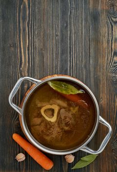Paleo bone broth diet, beef meat soup. Low-carb food, keto recipe. Rich broth of slow languishing on beef and bones, prolonged boiling. Long cooking in pan. Dark wooden table, vertical, copy space