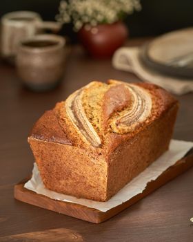 Banana bread. Cake with banana, traditional american cuisine. Whole loaf. Dark background, black table, shadows. Side view, close up.