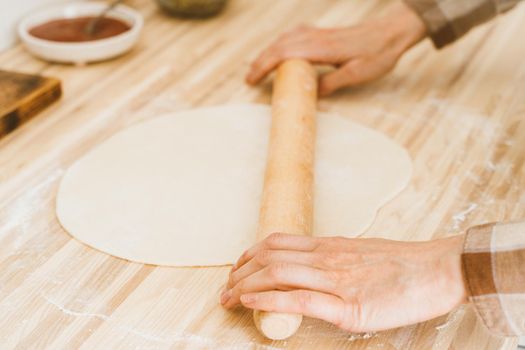 Faceless woman roll out dough with rolling pin on kitchen table at home, apartment, flour, scales, bowls, digital tablet with recipes on table. Homemade food