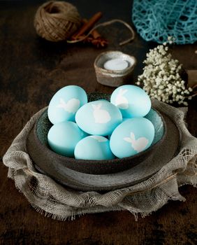 Unusual Easter on dark old background. Ceramic brown bowl with blue eggs. Darkness, rays of sunlight shine on eggs. Concept of new life, rebirth. Rustic style. Vertical, copy space