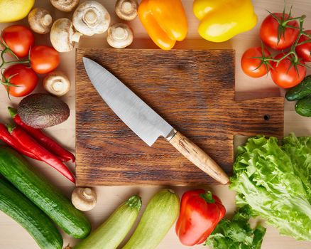 Vegetables around wooden cutting board with knife on kitchen table. Top view. Food ingredient background.