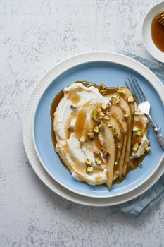 Ricotta with pears, pistachios and honey or maple syrup on blue plate on white table. Sweet and healthy dessert. Vertical