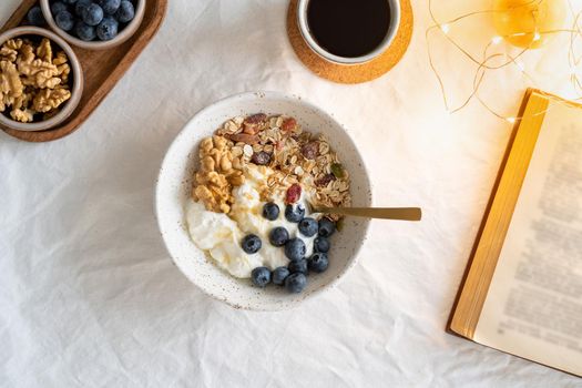 Top view book and Christmas healthy lifestyle breakfast with granola muesli and yogurt in bowl on white table background, cereal grain food with nuts seed. Organic morning diet meal with oat